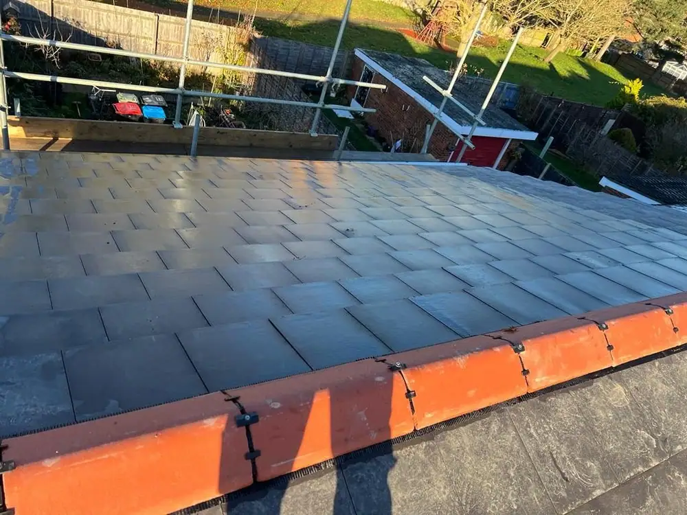 Finished slate-effect roof with terracotta ridge seen from the scaffold