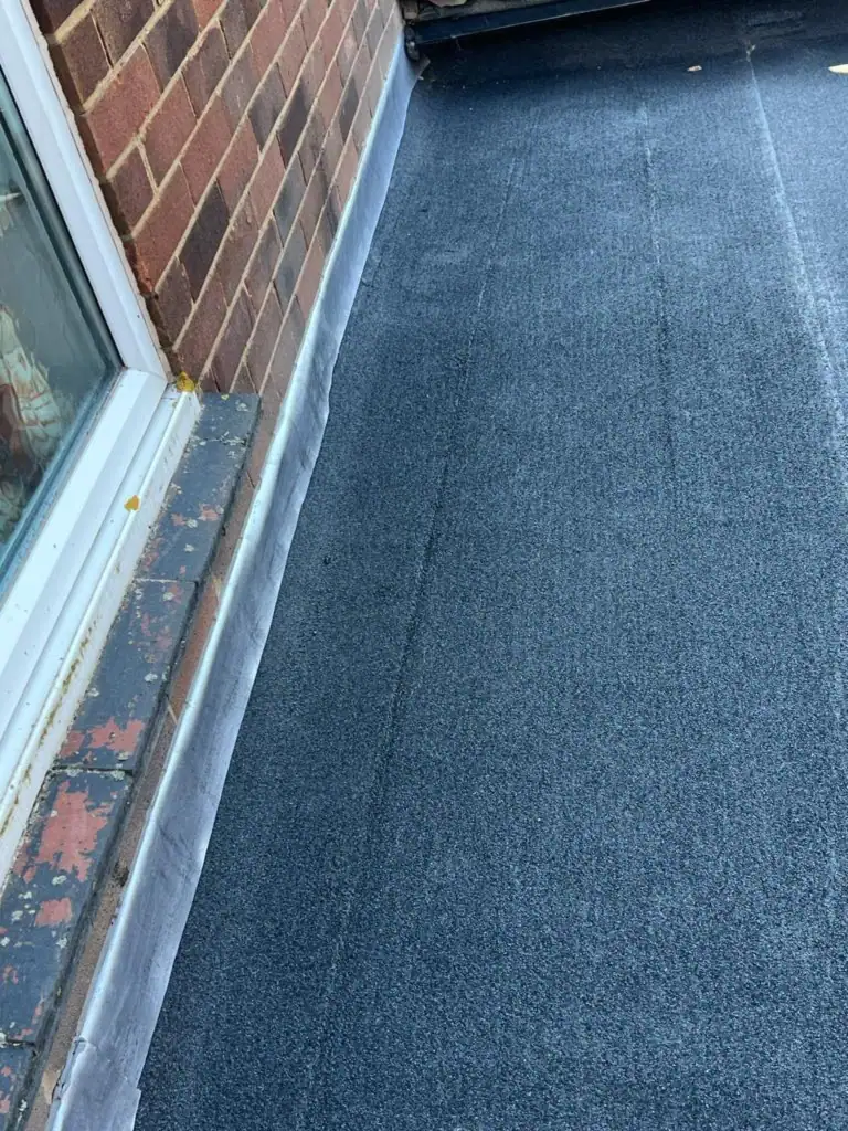New grey mineral felt flat roof dressed against a window and wall