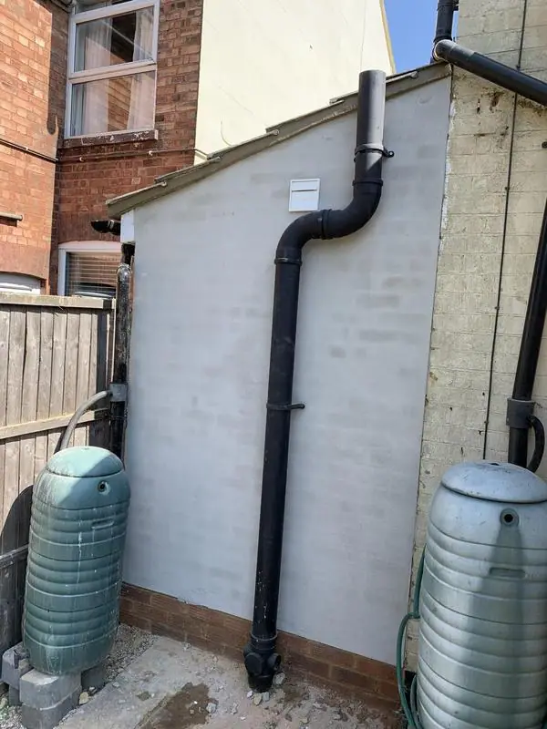 New black downpipe on a rendered extension with water butts