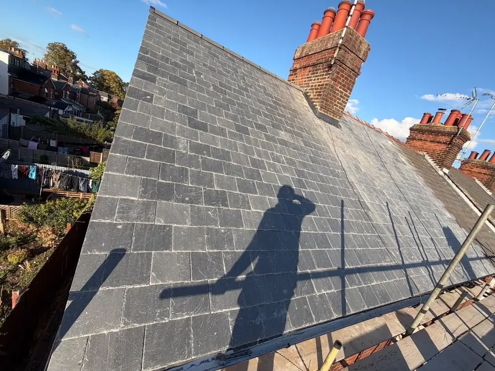 New slate roof slope running up to a chimney with terracotta pots