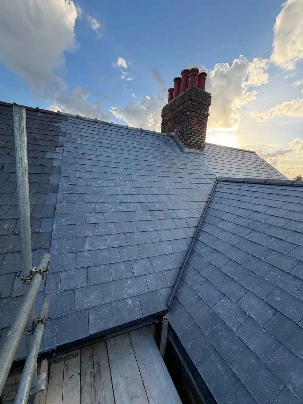 Slate roofing: new natural slate roof with a brick chimney and valley, seen from the scaffold
