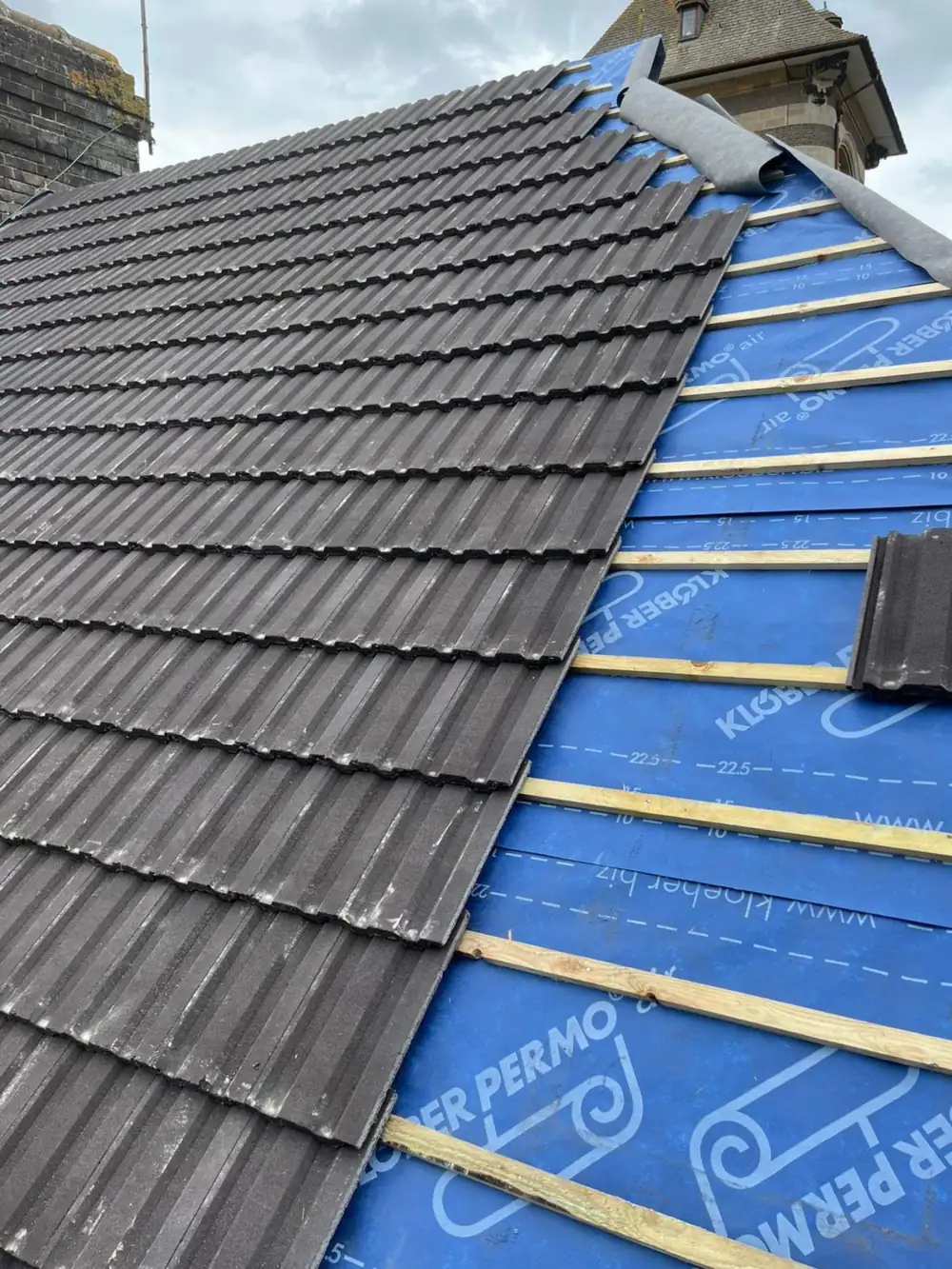 Roof repairs in London: new grey tiles laid beside blue Klober membrane and battens