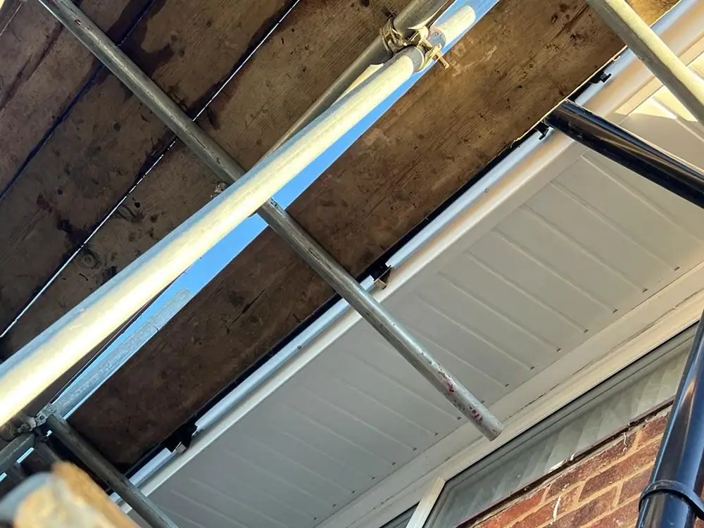 New white uPVC soffit being fitted under the eaves of a house with scaffold tubes in shot