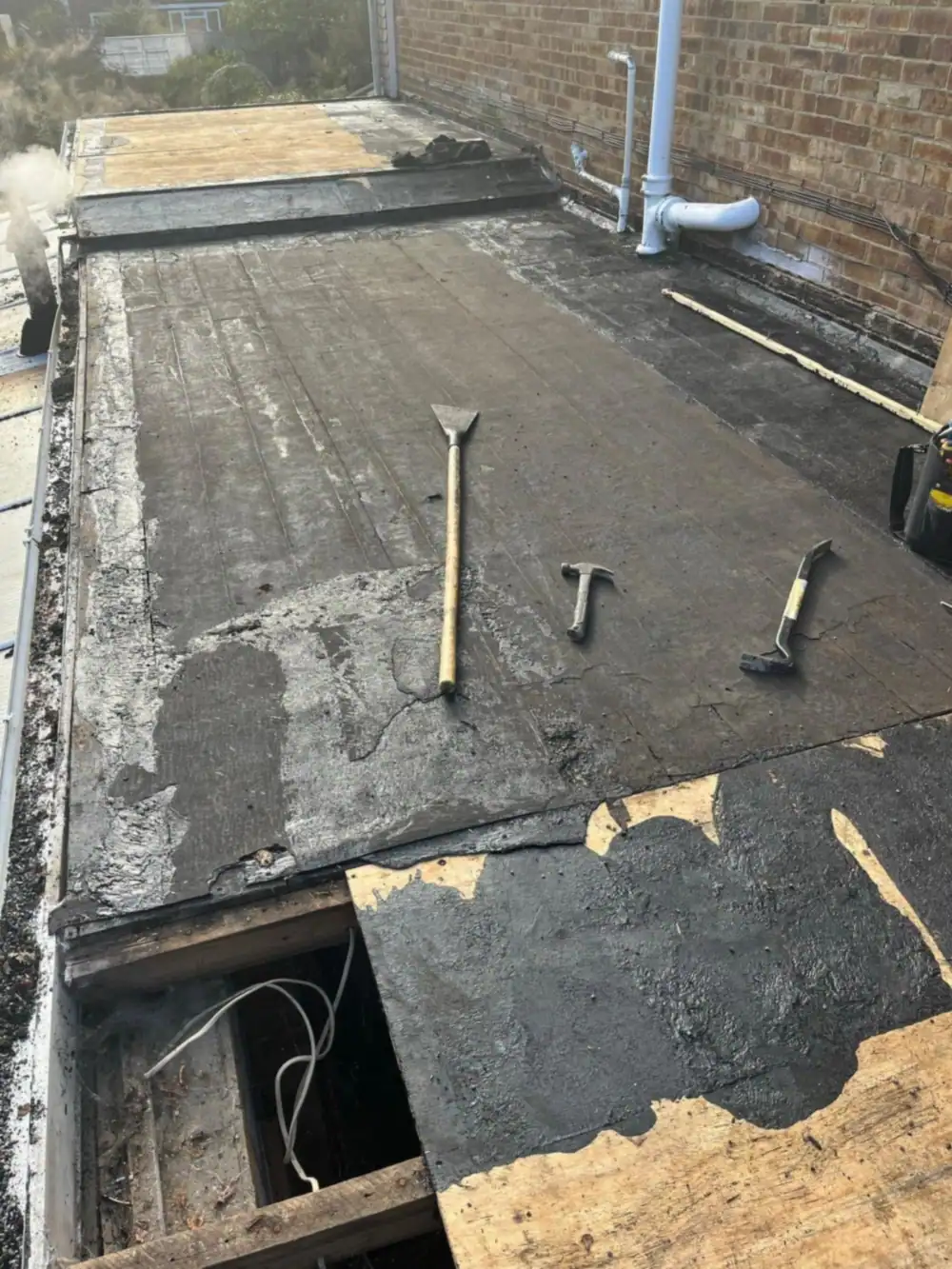 Old flat roof being stripped with tools on the deck
