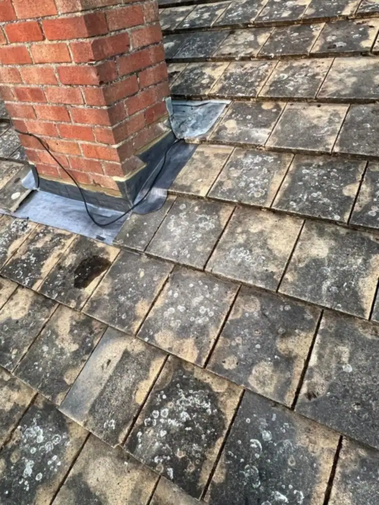 Lichen-covered tiles and old lead around a chimney before the re-roof, as seen on older roofs in Bedford