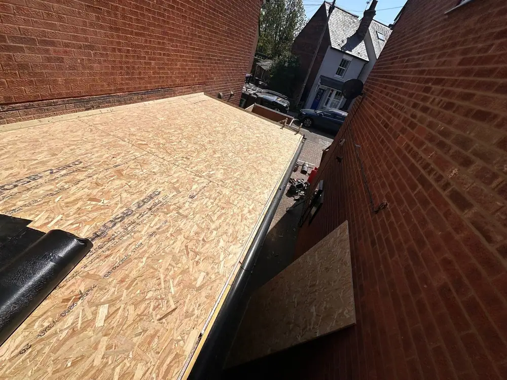 Garage roof replacement stage: a new OSB flat roof deck laid between two brick walls
