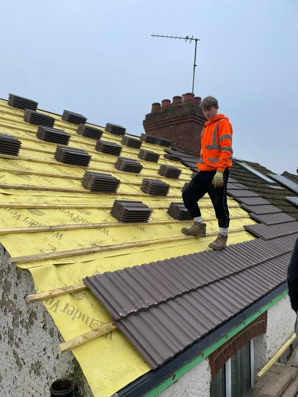 Roof tile replacement: roofer in hi-vis laying new tiles with tiles loaded out on the battens