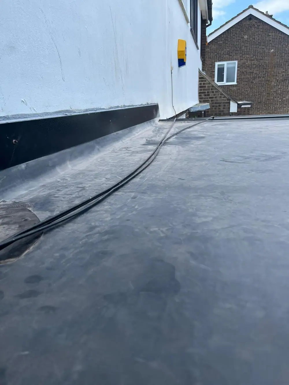 Finished rubber flat roof running along a white rendered wall