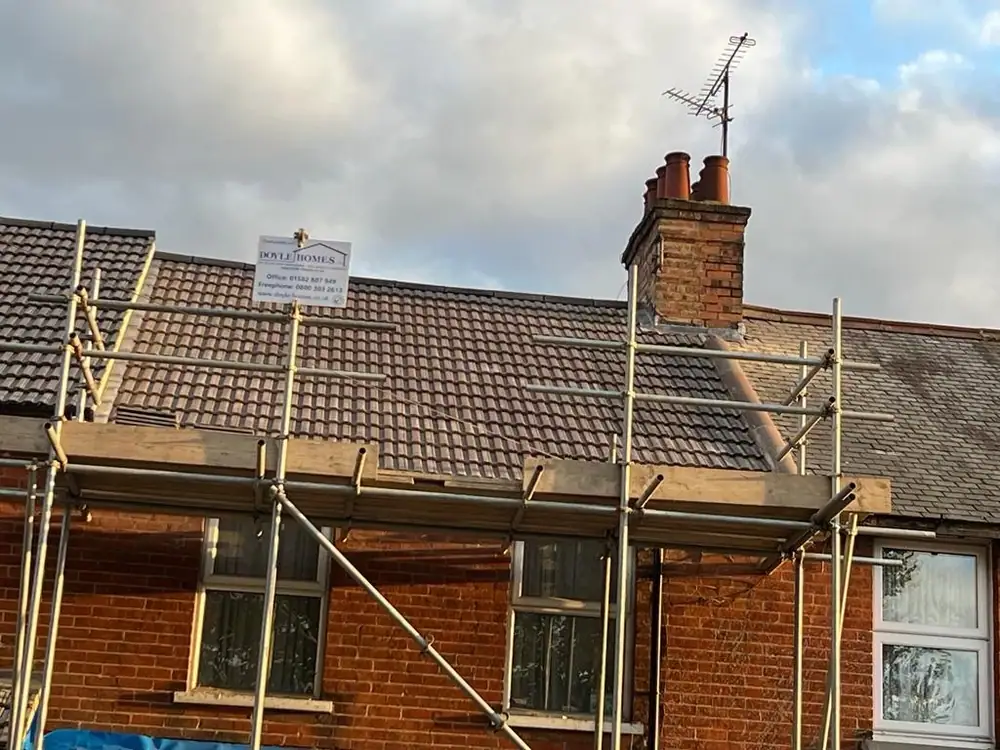 Emergency roof repair: a terraced house scaffolded for safe roof access with the Doyle Homes board in place