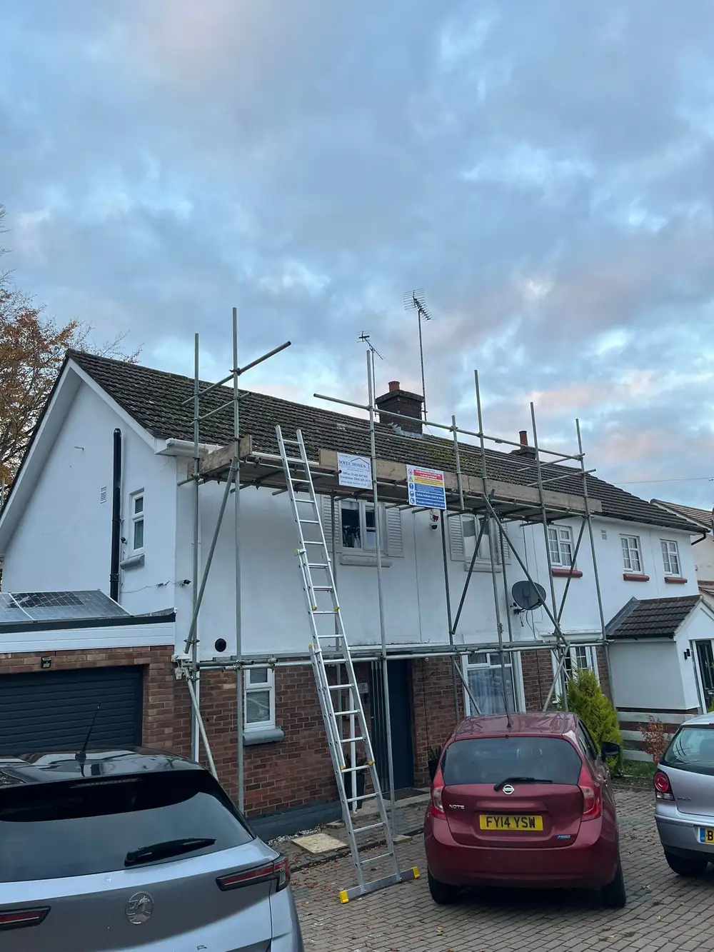 White rendered house scaffolded for a re-roof, cars on the drive